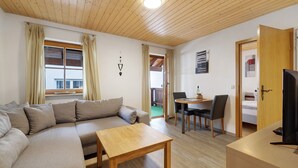 A modern living room with a sofa, a wooden coffee table, a dining area with a table and chairs, and a television on a stand. - Apartment 'Haus 3 2-zimmer' with Lake View, Shared Terrace and Wi-Fi (Meersburg)