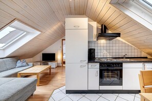 Una cocina moderna con horno empotrado, una zona de comedor con mesa de madera y un sofá gris.