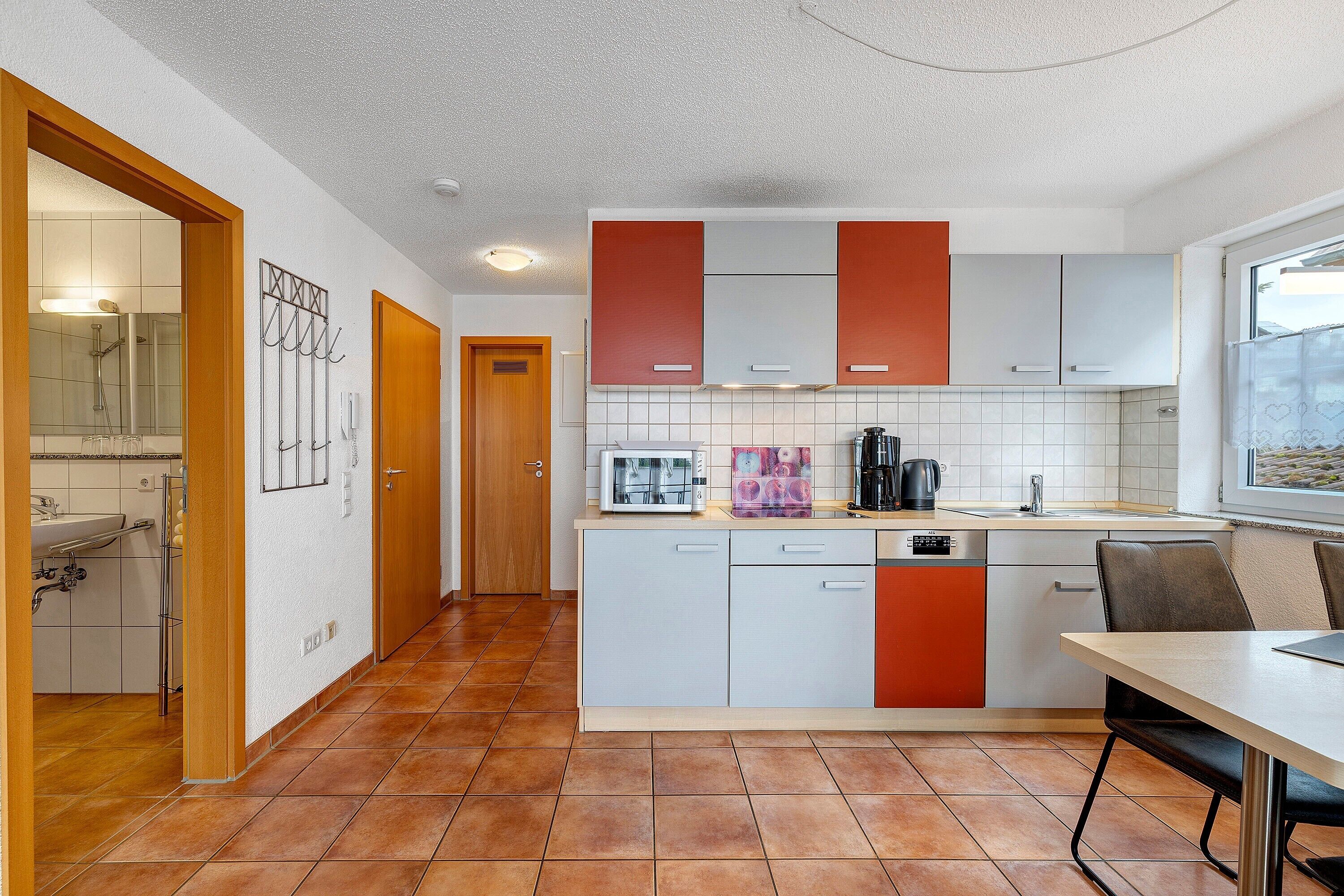 Une cuisine moderne avec des meubles blancs et orange, un four à micro-ondes, une machine à café et une fenêtre.