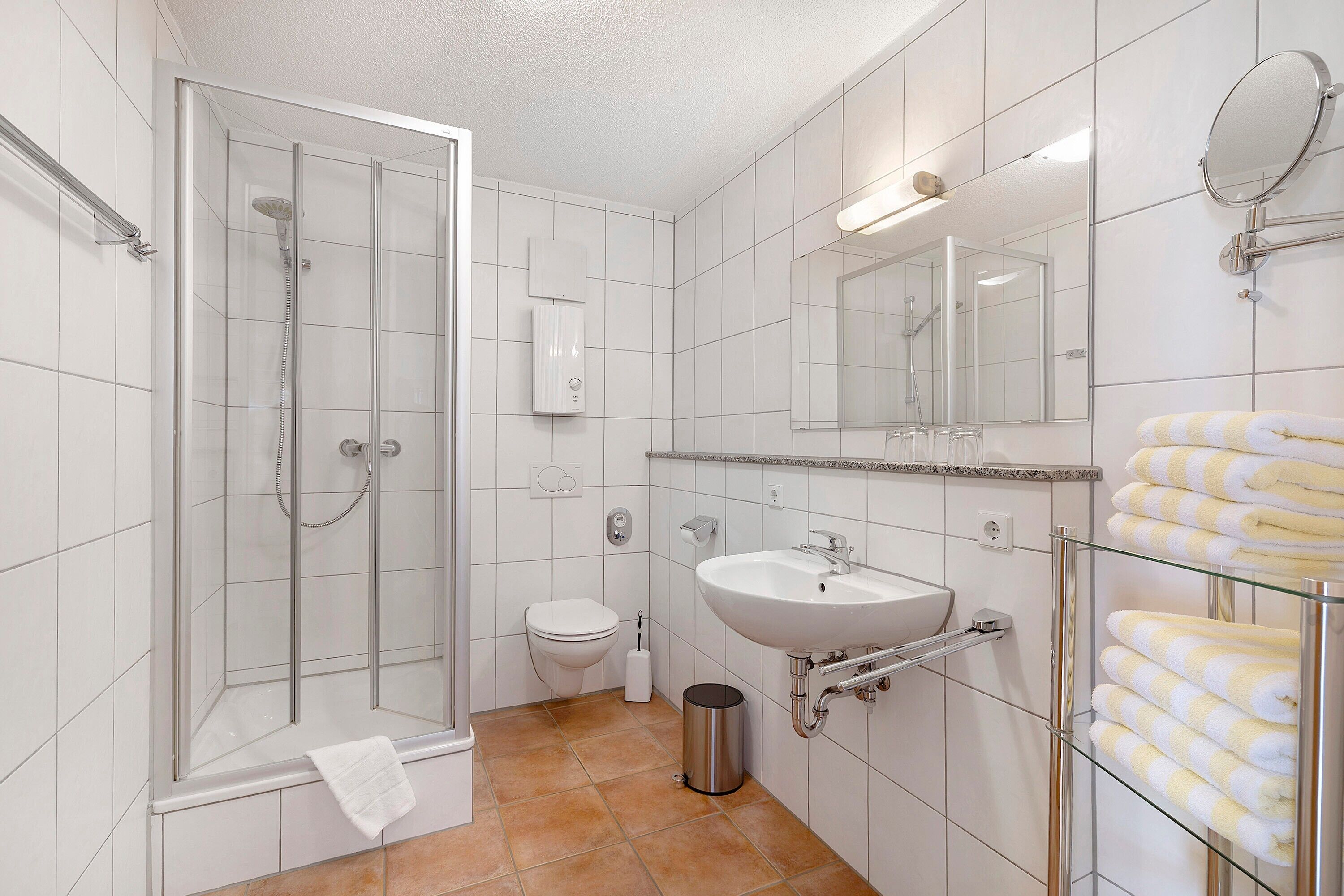 Un baño moderno con ducha de vidrio, un lavamanos blanco, inodoro y toallero de vidrio.