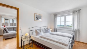 Un dormitorio con cama, una mesita de noche con lámpara, una ventana con cortinas y vistas al exterior.