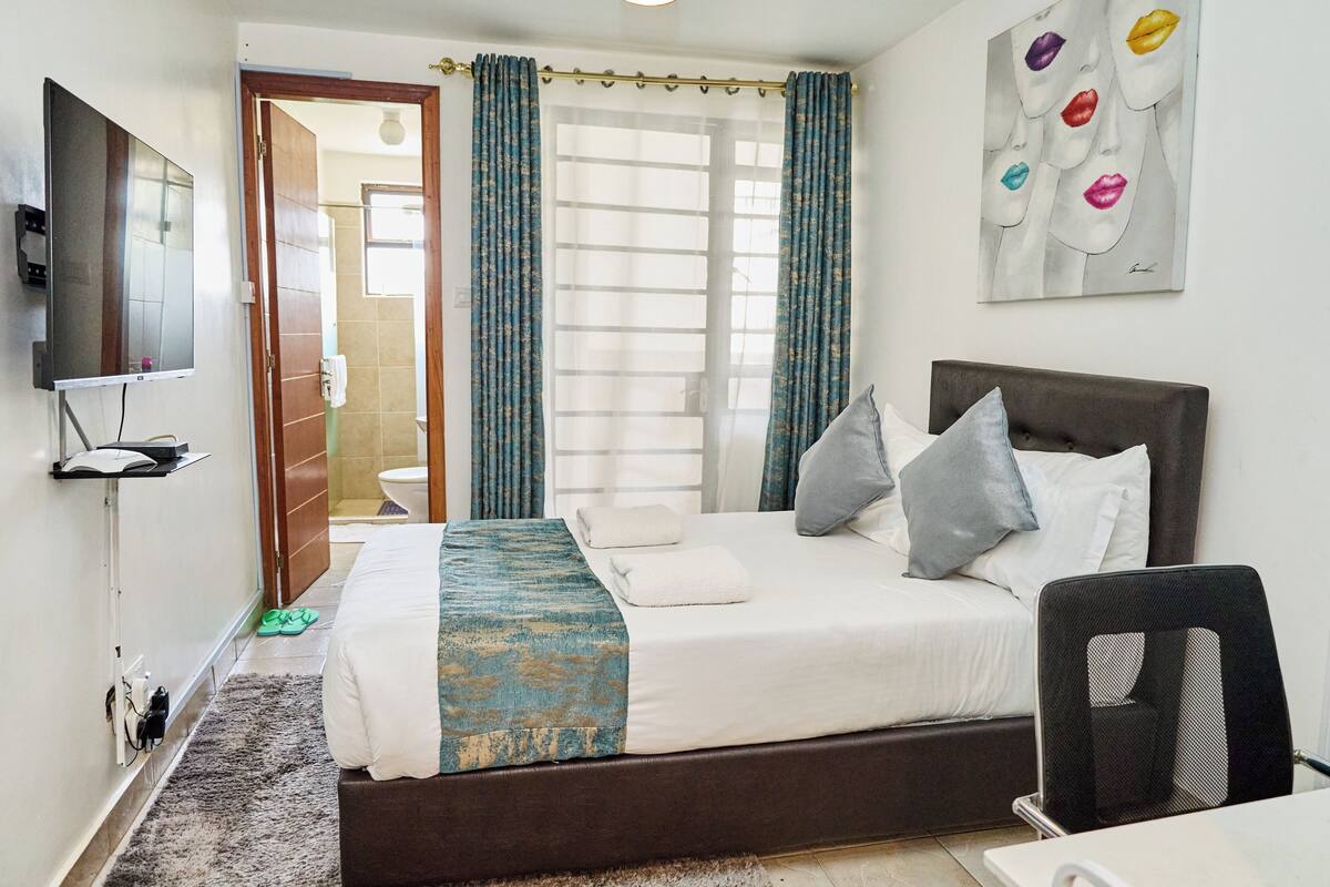A hotel room with a bed, a TV, a desk, and a chair.