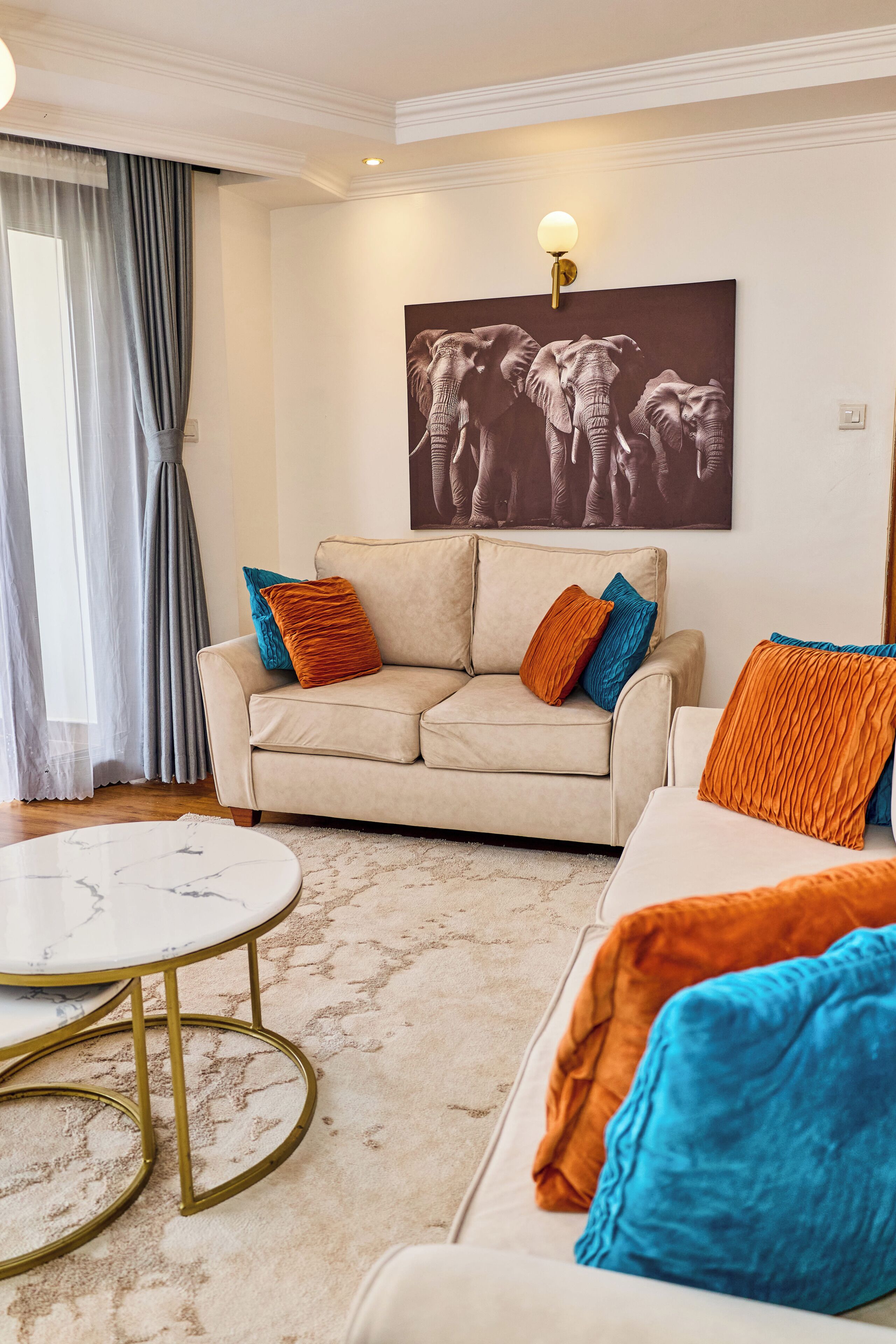 A living room with a beige sofa, a round coffee table, and a large elephant painting on the wall.
