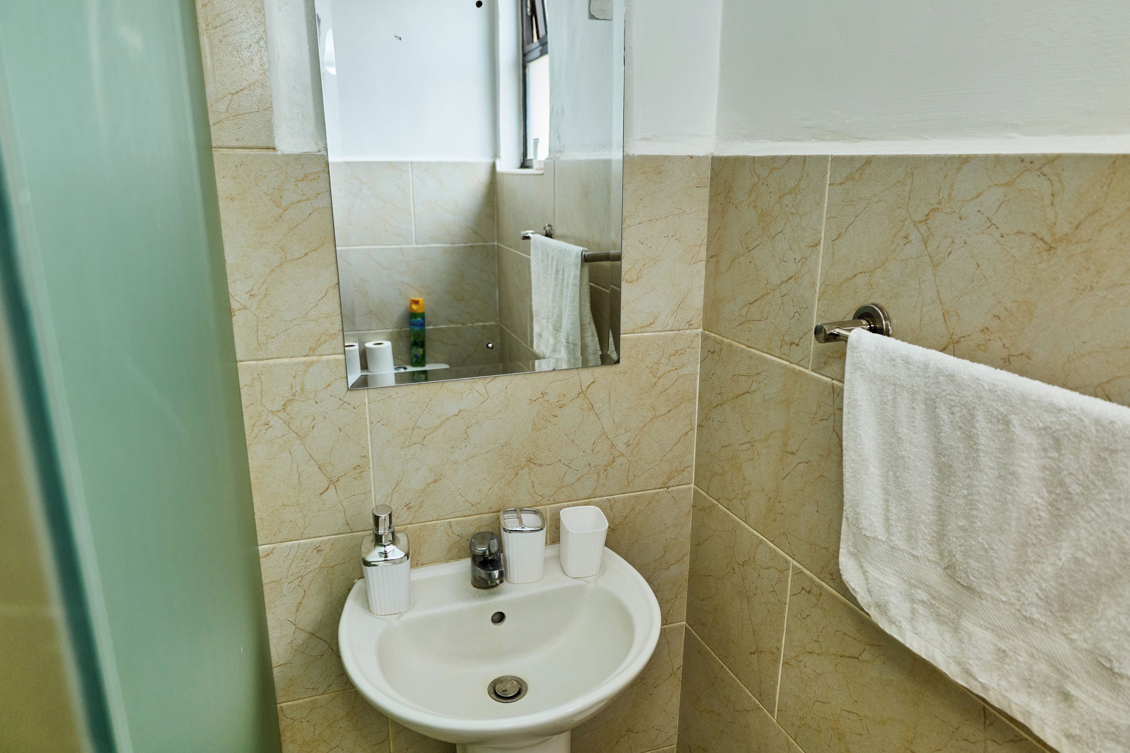 Un baño con lavamanos, espejo, toallero y artículos de aseo.