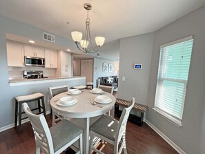 A modern kitchen with white cabinets, a central island, and a dining area with a round table and chairs.