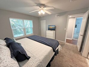 A bedroom with a bed, a ceiling fan, a TV on a dresser, and a window with blinds.