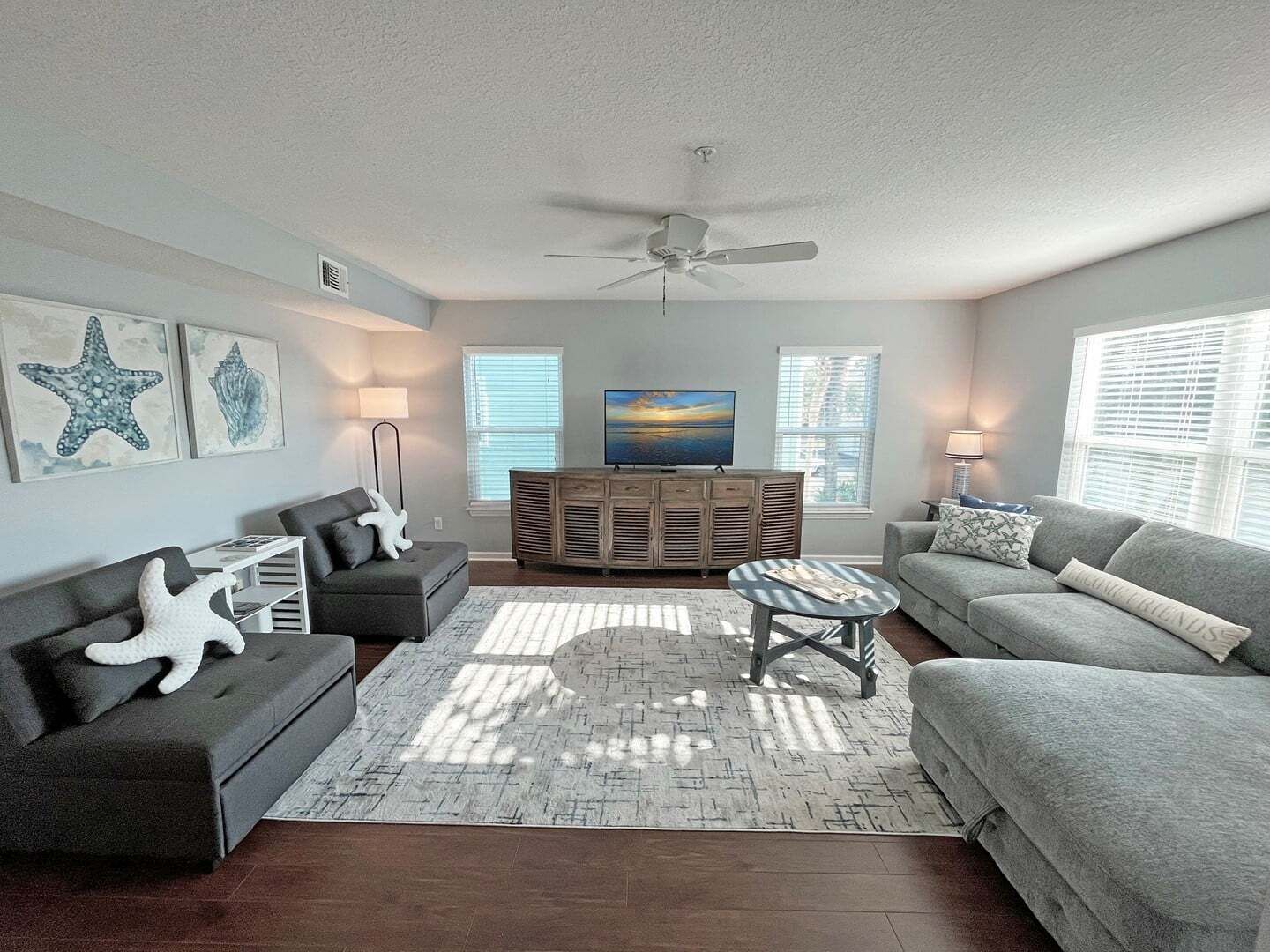 A living room with a grey sofa, a coffee table, a TV on a wooden cabinet, and starfish decorations.