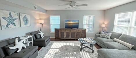 A living room with a grey sofa, a coffee table, a TV on a wooden cabinet, and starfish decorations.