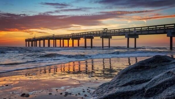 Um píer que se estende até o oceano, com o pôr do sol ao fundo.