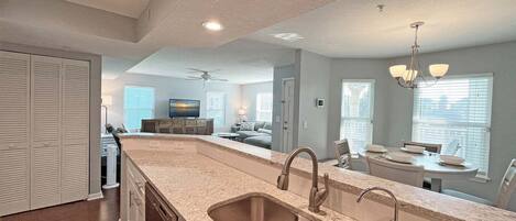 A modern kitchen with a granite countertop, stainless steel sink, and a dining area with a table and chairs.