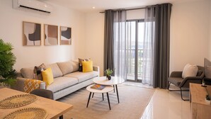 A modern living room with a grey sofa, a round coffee table, and a TV on a wooden stand. - One bedroom Luxury @ Loxwood…..Enjoy! (Accra)