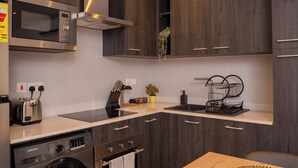 A modern kitchen with dark wood cabinets, stainless steel appliances, and a built-in washing machine. - One bedroom Luxury @ Loxwood…..Enjoy! (Accra)