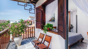 A balcony with wooden chairs, a potted plant, and a bed with a white curtain. - AuLac Hoian Homestay (Hoi An)