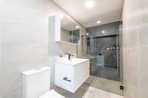 A modern bathroom with a glass-enclosed shower, a white vanity with a mirror, and a toilet.