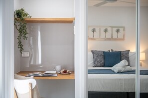Una habitación con una cama, un escritorio con una planta, una taza y un libro.