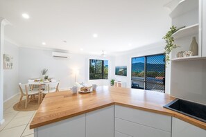 A modern kitchen with a wooden countertop, white cabinetry, and a dining area with a round table and chairs.