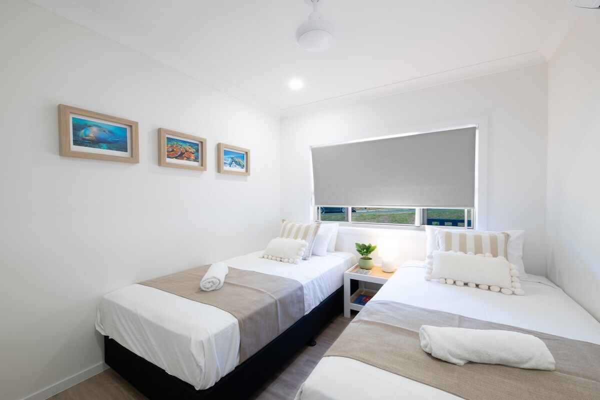 A bedroom with two beds, a window with a view, and three framed pictures on the wall.