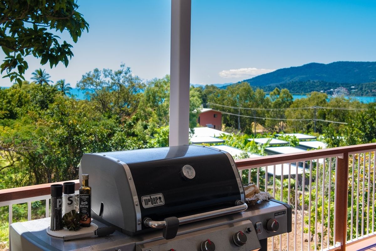 A Weber grill with condiments on a balcony overlooking a scenic landscape.