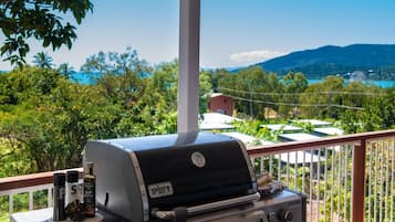 A Weber grill with condiments on a balcony overlooking a scenic landscape.