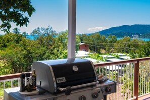 Churrasqueira Weber com acompanhamentos numa varanda com vista para uma paisagem deslumbrante.