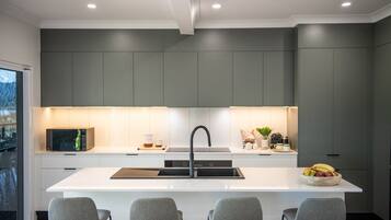 A modern kitchen with a central island, grey cabinetry, and a stainless steel sink.