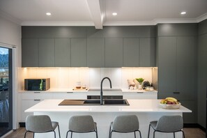 A modern kitchen with a central island, grey cabinetry, and a stainless steel sink. - Orana Coastal Retreat (Airlie Beach)