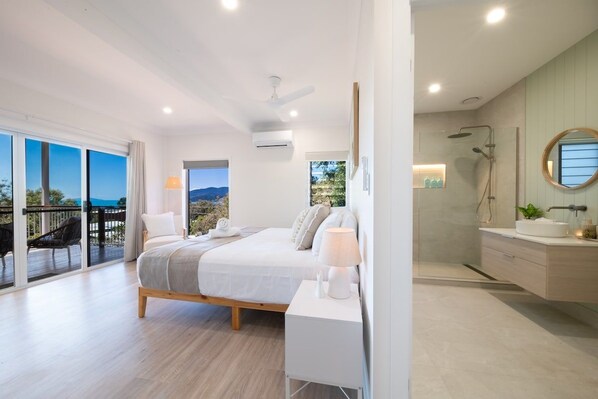 Quarto moderno com cama grande, mesa de cabeceira e vista para o exterior.