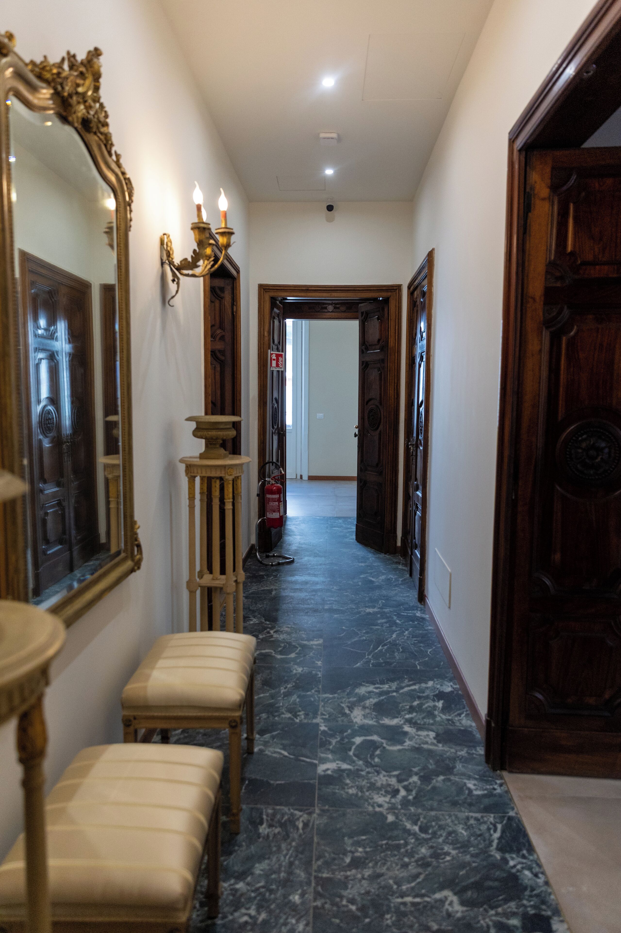 A hallway with a marble floor, a large ornate mirror, and a wooden bench.