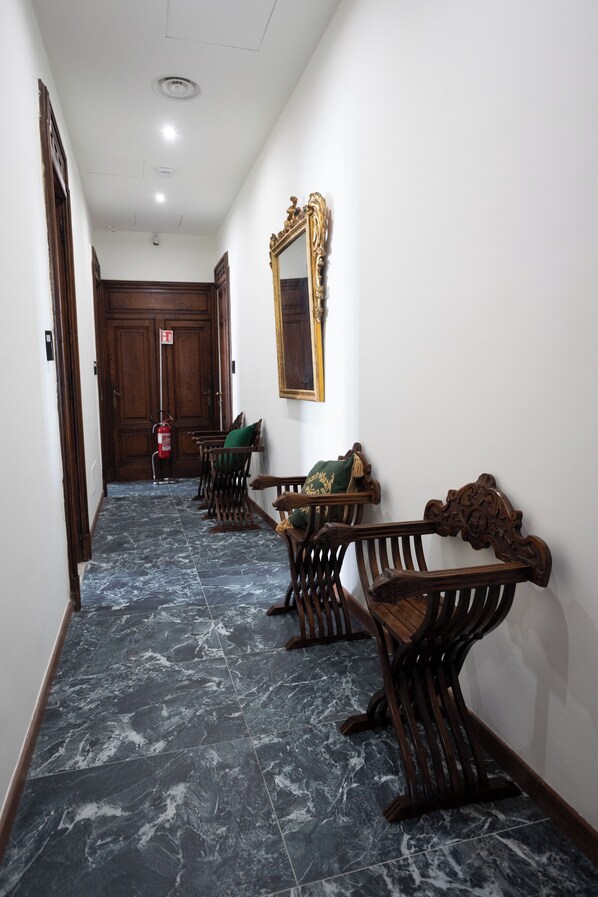 Un pasillo con bancos de madera, un extintor y una puerta al final.