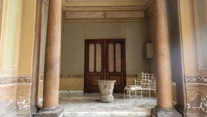 Un vaste hall d’entrée avec un sol en marbre, de grandes colonnes et une porte en bois.