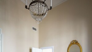 Une pièce avec un canapé blanc, un lustre, un miroir encadré d’or et une porte donnant sur une autre pièce.