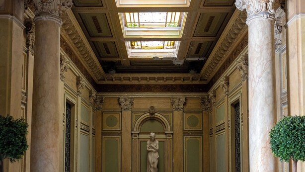 Un vaste hall d’entrée doté d’un sol en marbre, de colonnes richement décorées et d’une statue centrale.