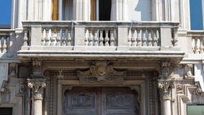 Une façade d’immeuble ornée de colonnes, une grande porte en bois et un portail en métal.
