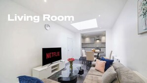A living room with a sofa, a glass coffee table, a flat-screen TV, and a small table with flowers. - Modern 3 Bed room Apartment with 4 Beds and 2 Full Bathrooms - Sleeps 6 (London)
