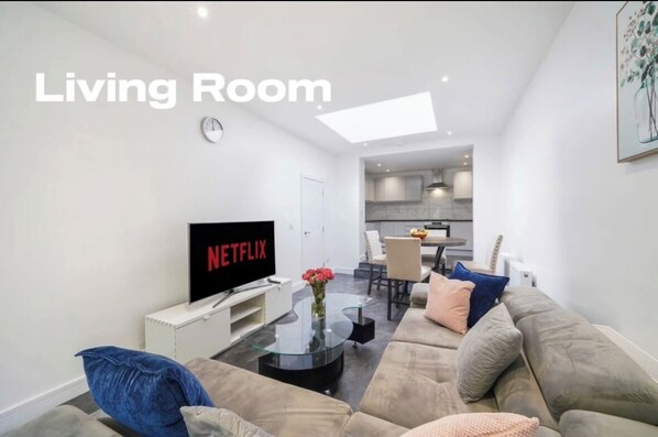 A living room with a sofa, a glass coffee table, a flat-screen TV, and a small table with flowers.