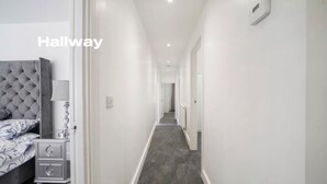 A hallway with a bed, nightstand, and lamp in a hotel room. - Modern 3 Bed room Apartment with 4 Beds and 2 Full Bathrooms - Sleeps 6 (London)