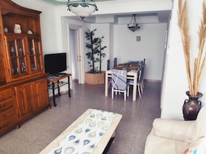 A living room with a TV, wooden cabinet, dining table, chairs, and a sofa.