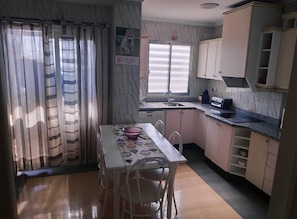 A compact kitchen with a dining table, chairs, a window with blinds, and a sink.
