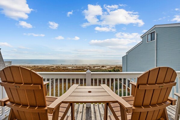 Une terrasse en bois avec deux fauteuils Adirondack donnant sur la plage.