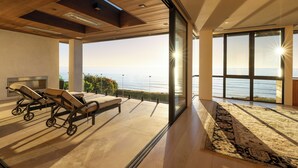 A modern room with a large window overlooking the sea, a sun lounger, and a patterned rug. - Luxury Coastal Escape w/ Resort-Style Amenities & Stunning Views (Del Mar)