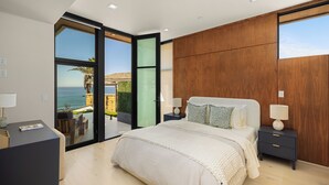 A modern bedroom with a large bed, wooden paneling, and a view of the sea. - Luxury Coastal Escape w/ Resort-Style Amenities & Stunning Views (Del Mar)