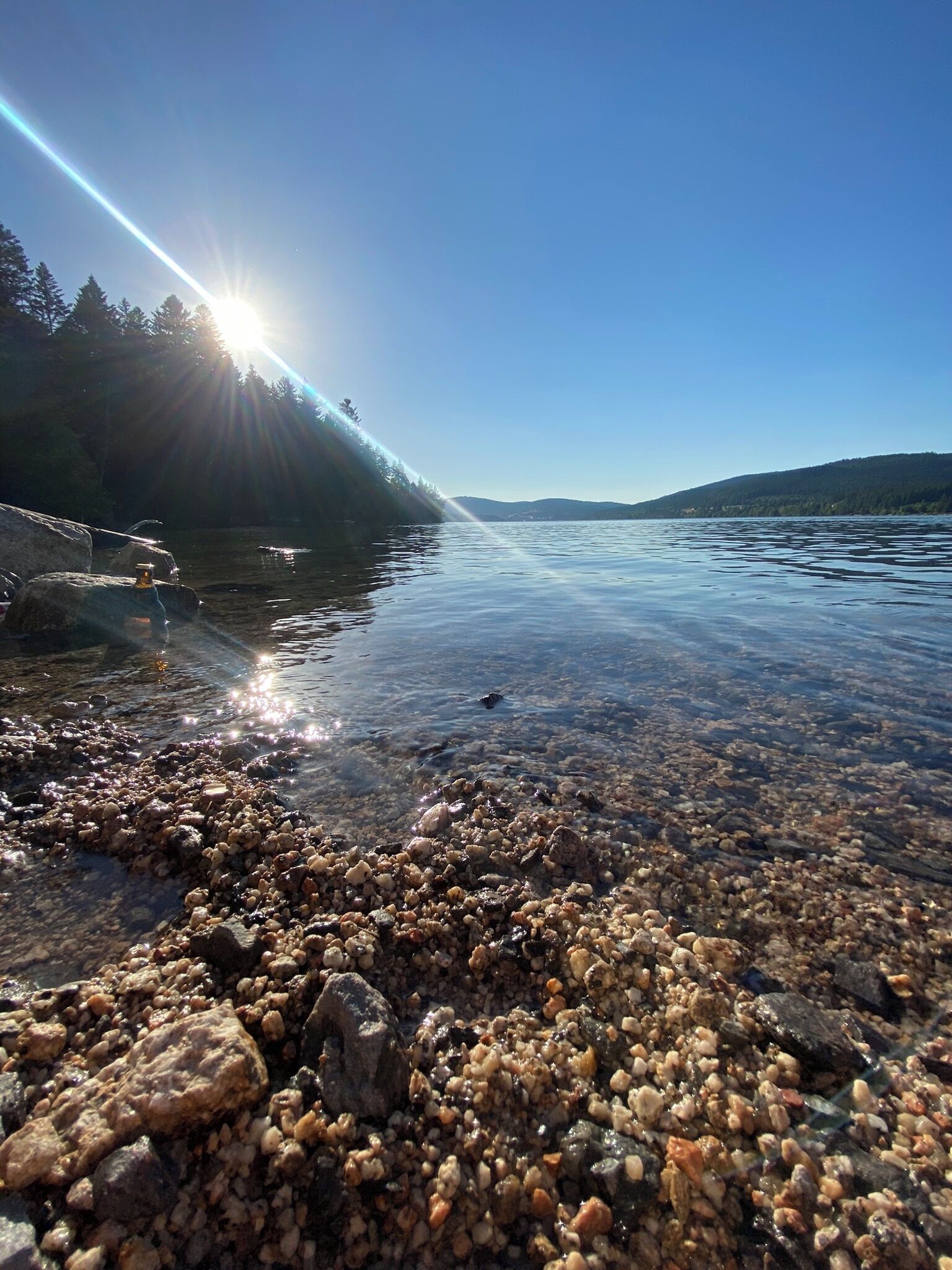 A clear lake with a rocky shoreline and a distant mountain range.
