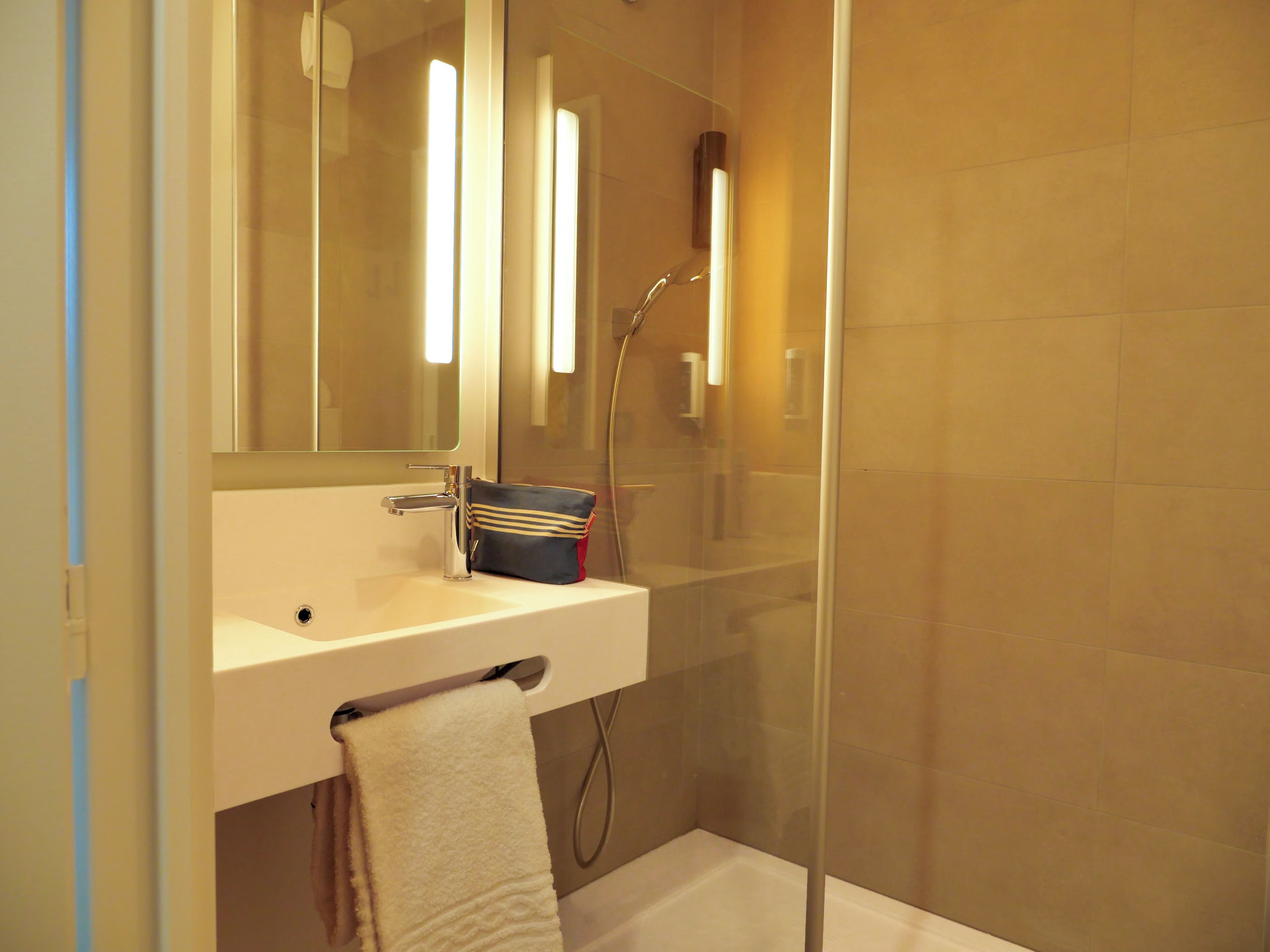 Une salle de bain moderne avec une douche à parois de verre, un lavabo blanc et une serviette accrochée au mur.