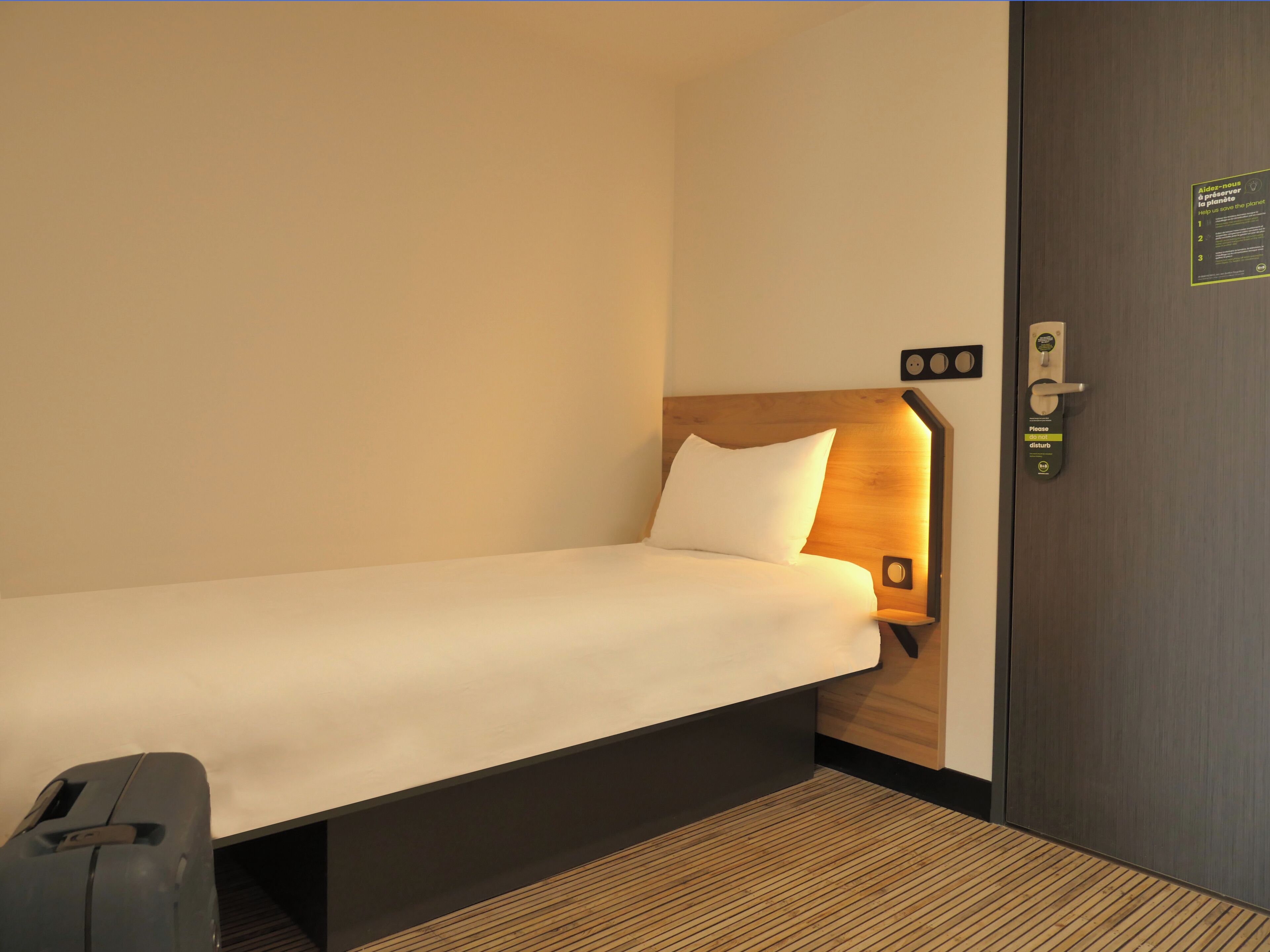 Ein Einzelbett mit Holz Kopfteil, ein Nachttisch und eine wandmontierte Bedienanlage.