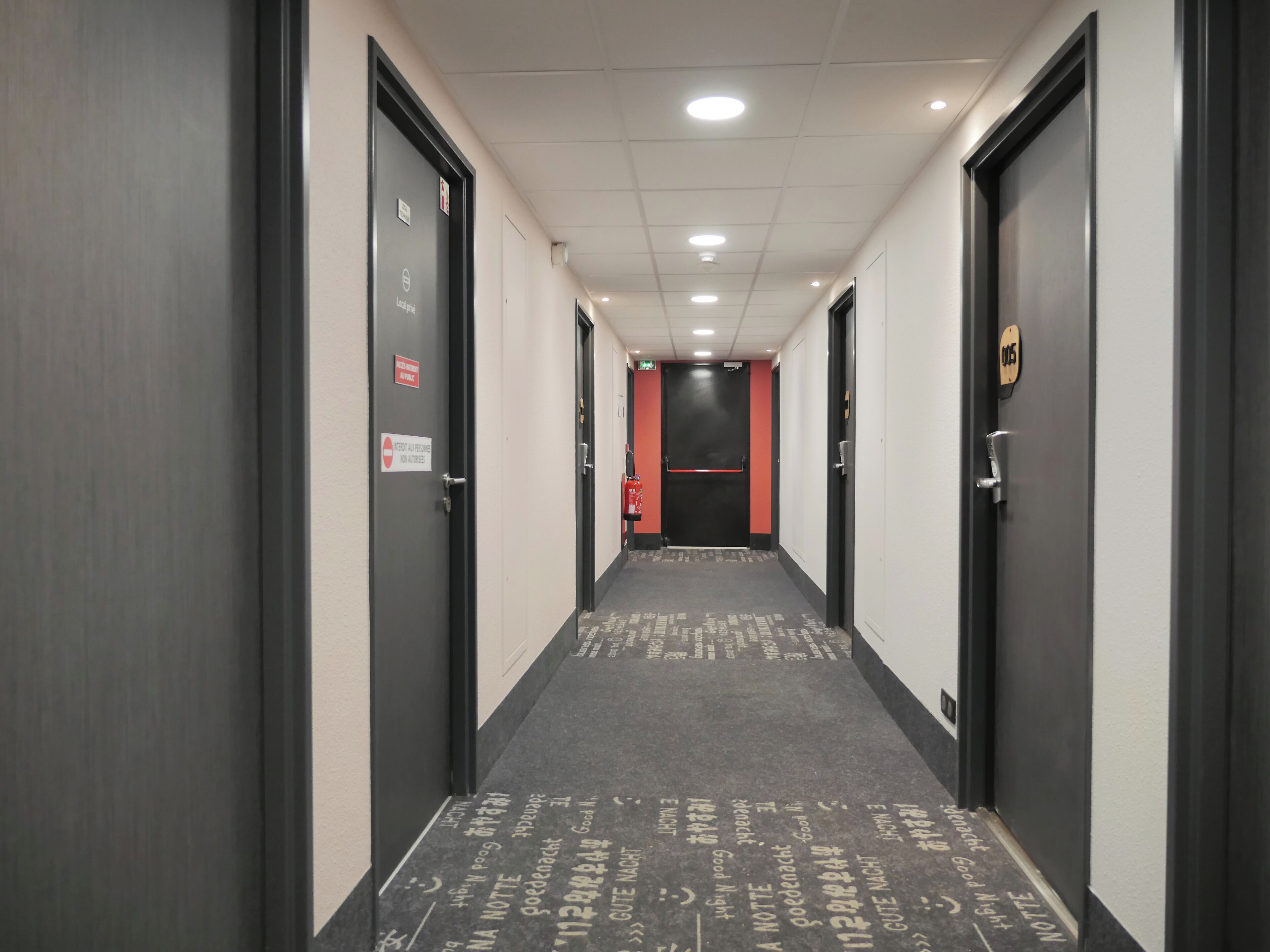 A corridor with doors on both sides, a red accent wall, and a carpet with text.