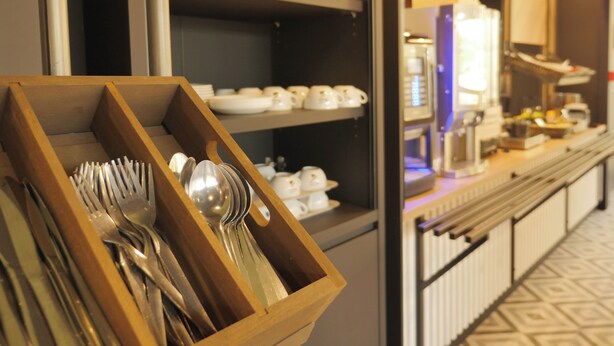 A buffet area with a wooden utensil holder, shelves with bowls and plates, and a counter with various food items. - BB HOTEL Carcassonne Rocadest La Cite (Carcassonne)