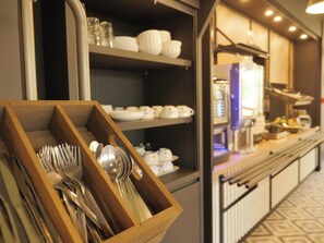 A buffet area with a wooden utensil holder, shelves with bowls and plates, and a counter with various food items. - BB HOTEL Carcassonne Rocadest La Cite (Carcassonne)
