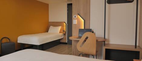 A hotel room with two single beds, a desk with a laptop, a chair, a coat rack, and a wall-mounted shelf.