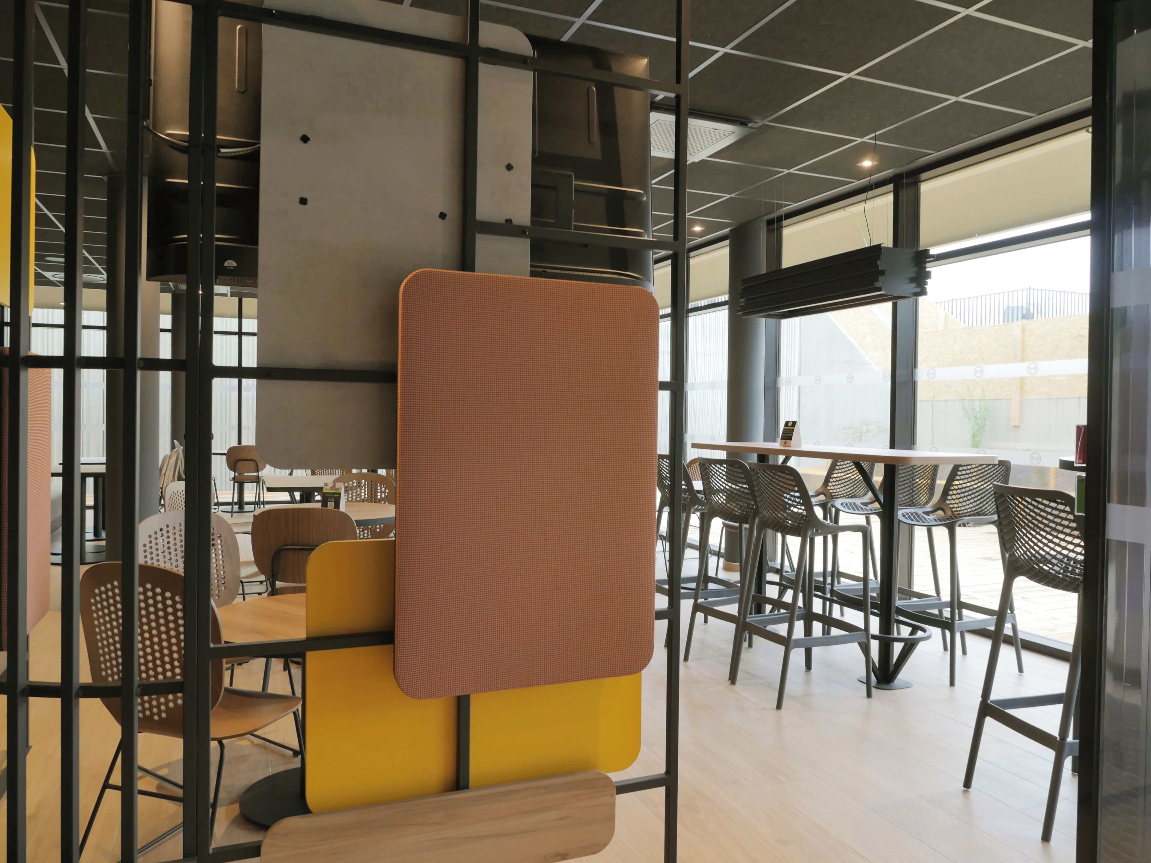 A modern indoor space with high ceilings, large windows, and a mix of seating arrangements including tables and chairs.