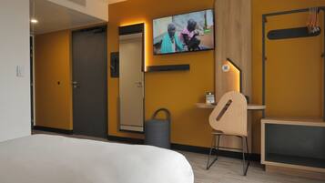 Een hotelkamer met een bed, een bureau met stoel, een aan de muur bevestigde televisie en een houten kast.